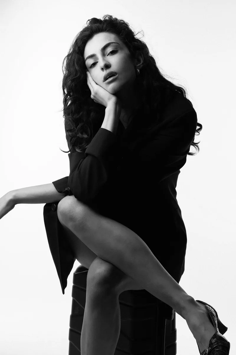 Elvin Köse, black and white studio portrait, seated with heels