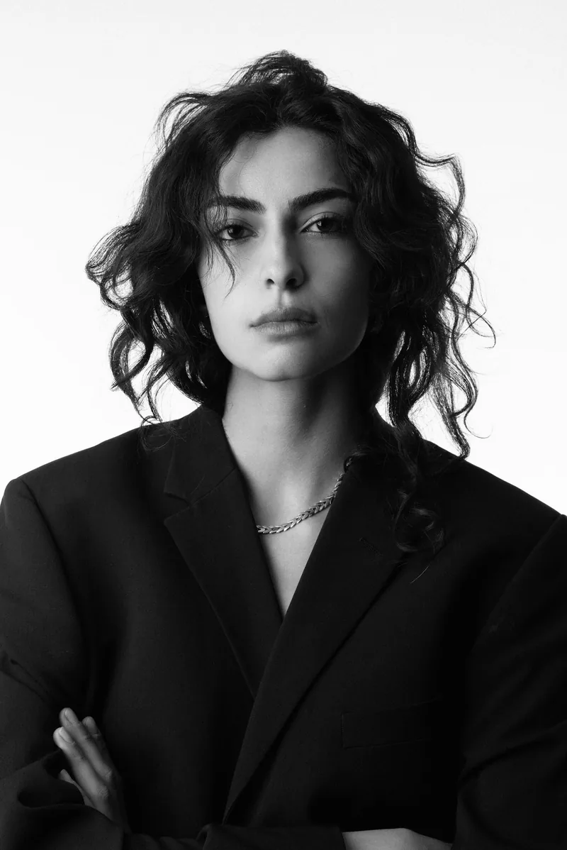 Elvin Köse, black and white studio portrait in a black blazer, facing the camera