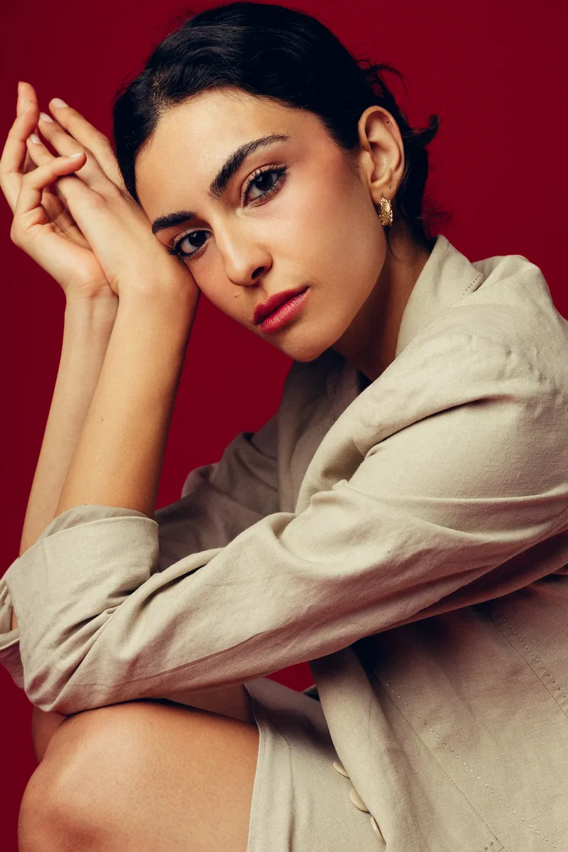 Elvin Köse, editorial portrait on a red backdrop, hands raised