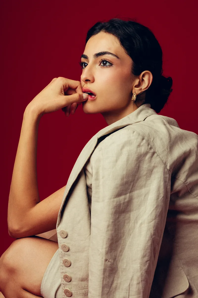 Elvin Köse, editorial portrait on a red backdrop, in profile with a hand at her chin