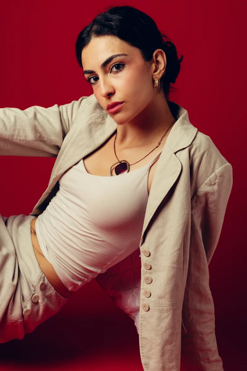 Elvin Köse, editorial portrait on a red backdrop, reclining in a linen jacket