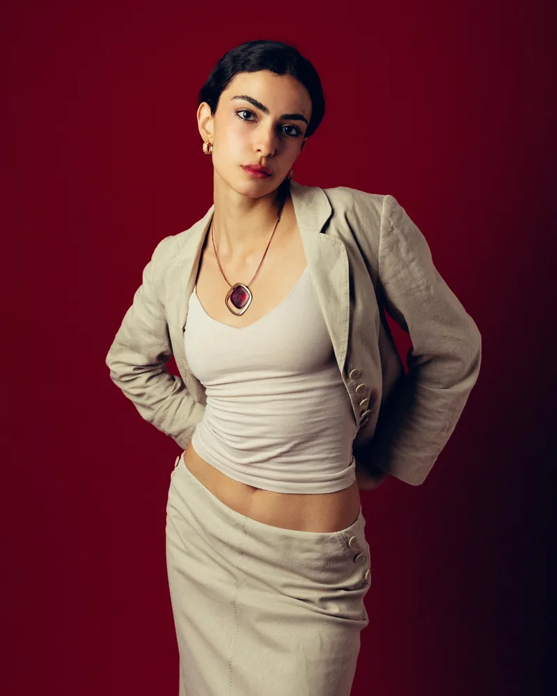 Elvin Köse, editorial portrait on a red backdrop, hands on hips