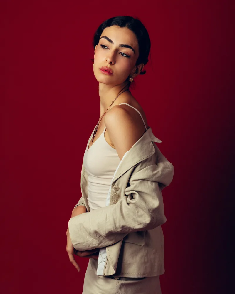 Elvin Köse, editorial portrait on a red backdrop, jacket off one shoulder
