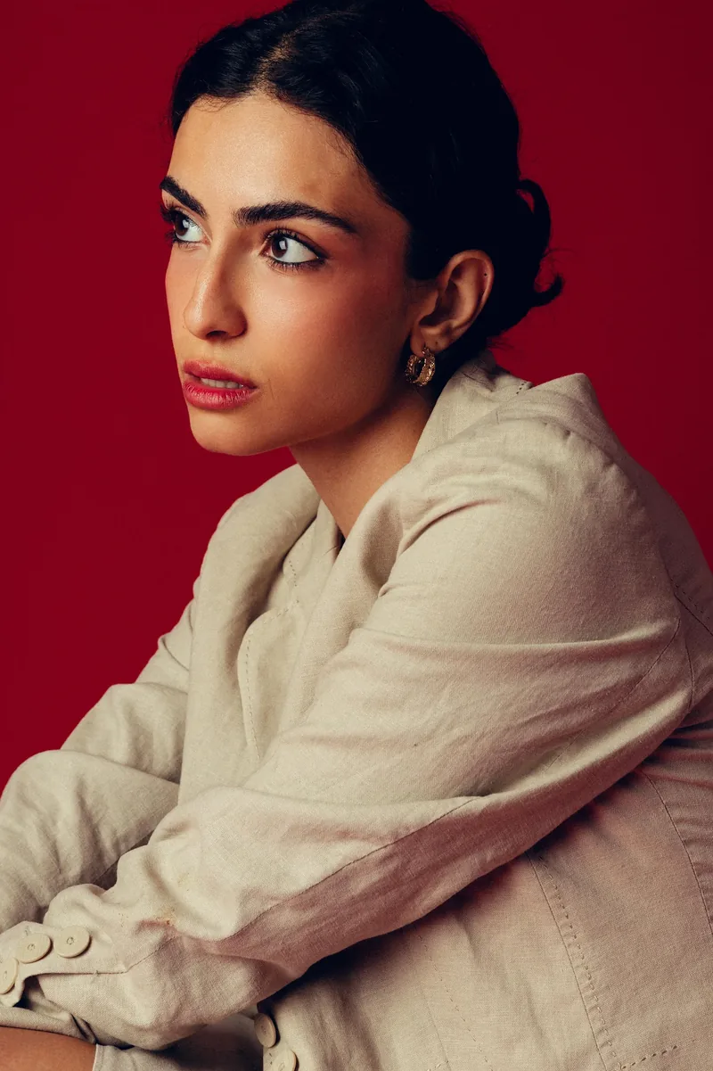 Elvin Köse, editorial portrait on a red backdrop, arms folded, looking away