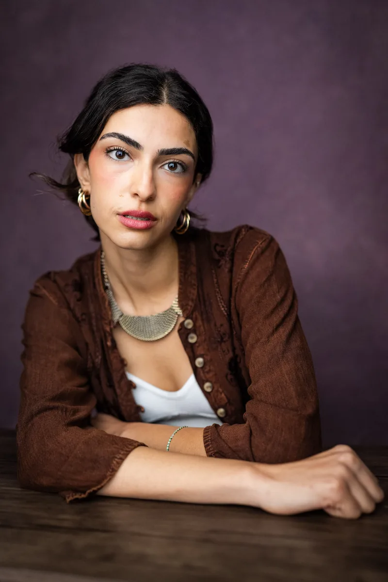 Elvin Köse, portrait in a brown cardigan against a plum backdrop